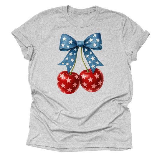 A casual short-sleeve unisex T-shirt in a light color, featuring a design of two red cherries with a stars pattern, tied with a blue ribbon with stars, celebrating a patriotic theme.