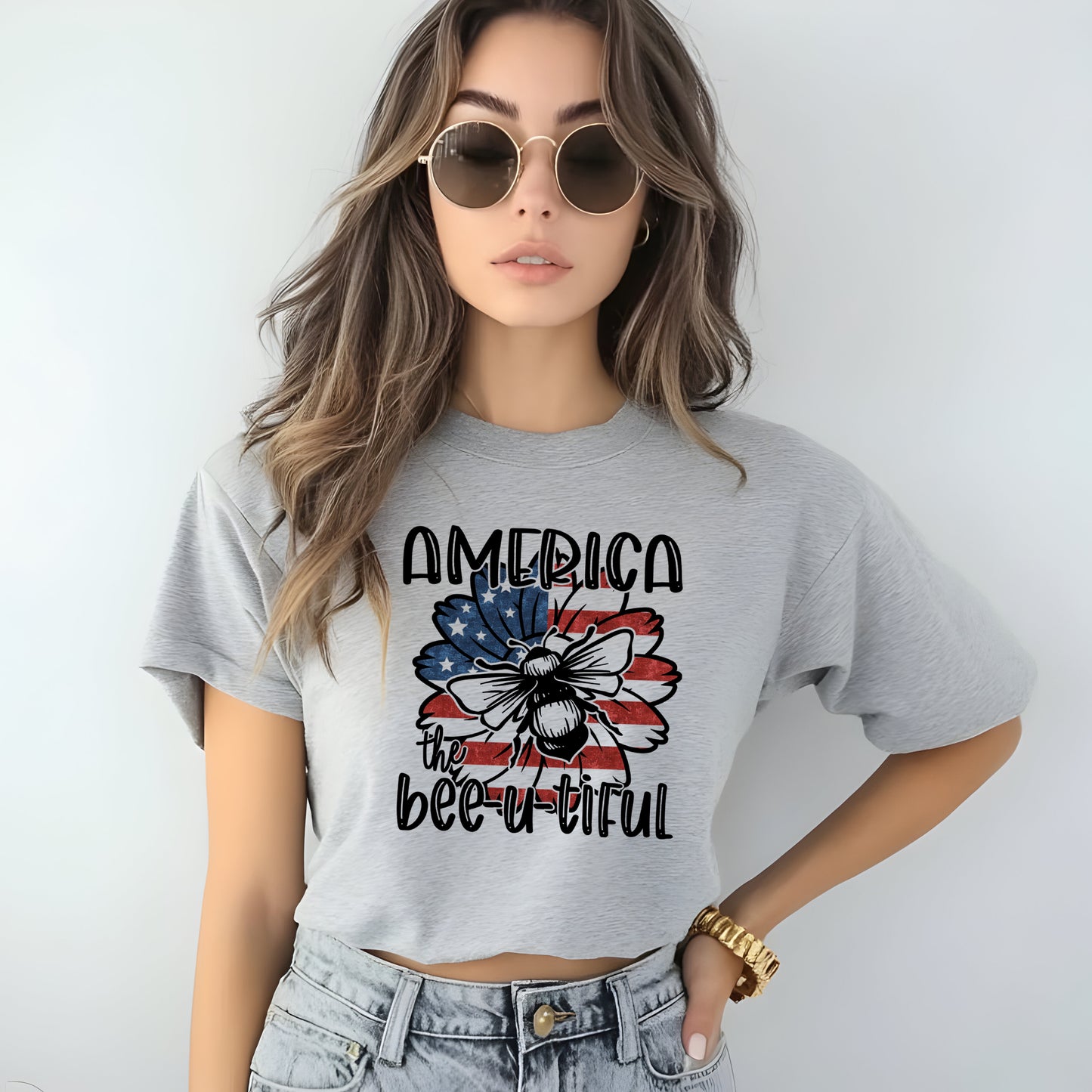 Woman wearing a gray t-shirt with 'America the bee-u-tiful' design with sunflower with american flag graphic with bee